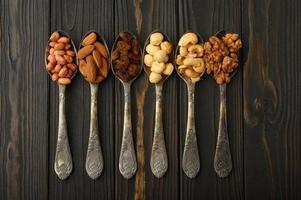 Hazelnut, cashews, raisins, almonds, peanuts, walnuts in silver spoons on a rustic background photo