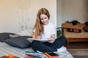 The girl after school plays at home, draws with pencils and felt-tip pens photo