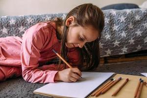 la niña después de la escuela juega en casa, dibuja con lápices y rotuladores foto