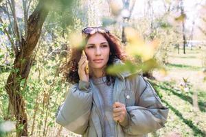 Young brunette woman talking on the phone in spring in the park photo