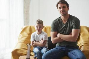 haciendo cara graciosa. padre y su hijo sentados juntos en el sofá. guitarra acustica en la cama foto