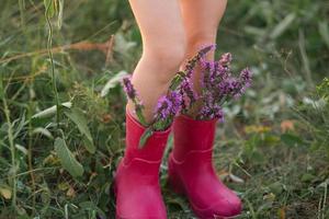 Red rubber boots on the feet of a girl with a bouquet of wild flowers. Flowers in a boot, summer time. Summer, freedom, nature, countryside, green grass in the field photo