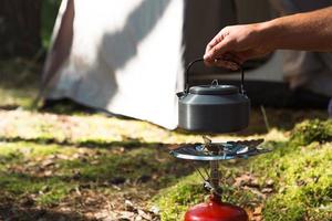 Cooking, heating a tourist kettle on a portable gas burner with a red gas cylinder. Camping, a man cooks breakfast outdoors. Summer outdoor activities photo