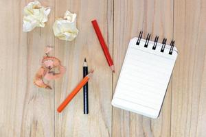 Small note book paper or notepad for writing information with color pencil and crumpled paper balls on wooden table. view from above photo