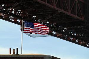 bandera estadounidense ondeando en el viento junto al puente golden gate en san francisco, california foto