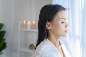 Portrait of young smiling asian beautiful woman wearing white bathrobe after finishing a shower photo