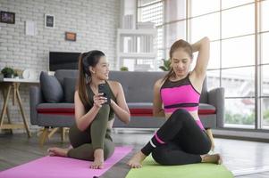 Young friend women practicing yoga at home unsing smart phone via online class with professional instructor, sport and healthy lifestyle concept. photo