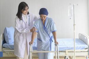 médico que ayuda a una paciente con cáncer que usa pañuelo en la cabeza con un andador en el hospital, atención médica y concepto médico foto