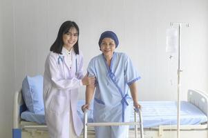 Doctor helping cancer patient woman wearing head scarf with walker at hospital, health care and medical concept photo