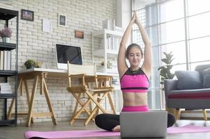 mujer joven en forma practicando yoga en casa a través de clases en línea con instructor profesional, deporte y concepto de estilo de vida saludable. foto