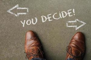 A man deciding on his future - looking down at the words You Decide written on the floor with arrows pointing in opposite directions photo