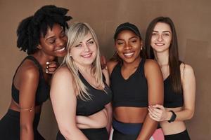 retrato de amigos alegres. grupo de mujeres multiétnicas de pie en el estudio con fondo marrón foto