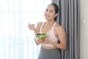 mujer joven en forma con ensalada después de hacer ejercicio en casa, deporte y concepto de estilo de vida saludable. foto