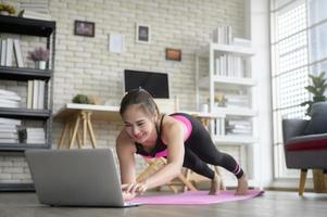 mujer joven en forma practicando yoga en casa a través de clases en línea con instructor profesional, deporte y concepto de estilo de vida saludable. foto