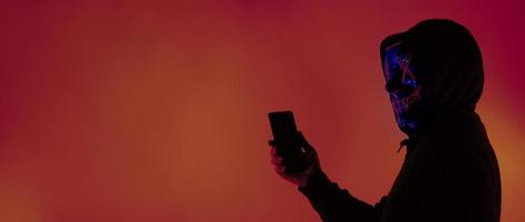 Anonymous hacker and face mask with smartphone in hand. photo