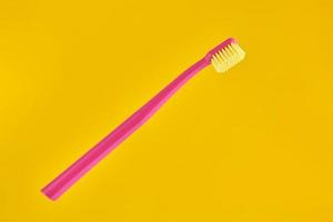 Pink toothbrush on yellow background for oral hygiene to clean teeth, gums and tongue photo