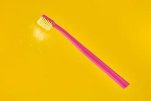 Pink toothbrush on yellow background for oral hygiene to clean teeth, gums and tongue photo