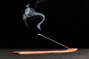 Smoke curls of burning incense stick in wooden holder for relaxation and meditation black background photo