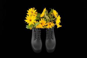 Black women platform boots with bouquet of yellow Jerusalem artichoke flowers, black background photo