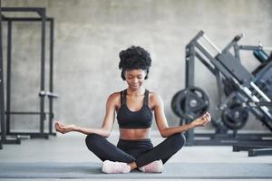 Meditation and relaxation. African american woman with curly hair and in sportive clothes have fitness day in the gym photo