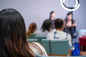 la audiencia y los participantes escuchan al profesor y al disertante al frente del escenario sobre el maquillaje facial de las mujeres. foto