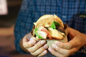 man's hand take big hamburger bacon, hold and ready to bite it in his mouth, at Thailand foodtruck event. photo