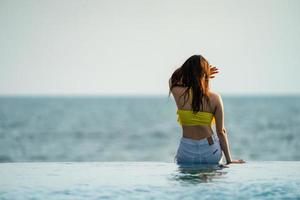 Asian Thai teenager female in Yellow relax and swim suit is posting on the infinity pool beside the sea beach in Thailand resort. photo