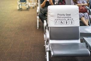 asiento prioritario blanco y gris cerca de la puerta de enlace del aeropuerto, con pasajeros borrosos detrás. idioma tailandés y chino significa asiento de prioridad foto