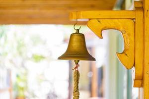 campana de latón con la mano en el palo grande de madera en la pared del poste. foto