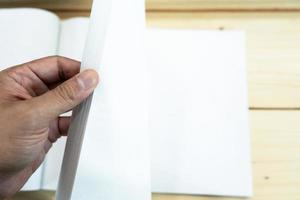 la mano del hombre abre el cuaderno blanco vacío en la mesa de madera. foto