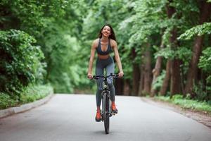 ciclista femenina en una bicicleta en una carretera asfaltada en el bosque durante el día foto