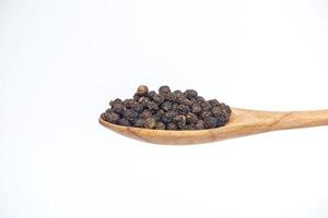Black pepper in the wooden spoon isolated on a white background. photo
