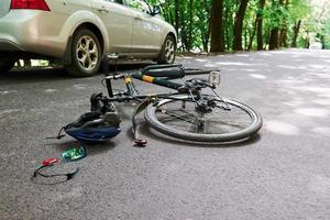 Damaged equipment. Bicycle and silver colored car accident on the road at forest at daytime photo