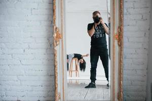 Showing hello. Man with camera taking a shot in the vintage mirror. Girl is having fun behind photo