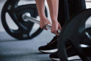 Cropped photo of woman doing squatting with barbell in the gym