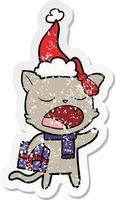 distressed sticker cartoon of a cat with christmas present wearing santa hat vector