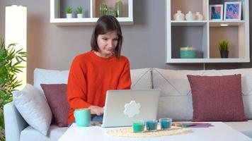 Woman working at computer drinking coffee.  Relaxed young woman using computer browsing social media, checking news, playing mobile games or texting sitting on sofa. video