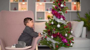 celebración del año nuevo del bebé. bebé juega con adornos en el árbol de navidad y celebra el año nuevo. video