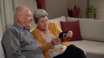 Old age and happy news. Elderly couple making a video call with their grandchildren on the phone. Grandfather and grandmother who are longing for their children. Sadness, Happiness.