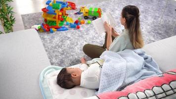 moeder die een boek leest en haar slapende baby. de moeder leest een boek naast haar baby en bedekt haar baby. video