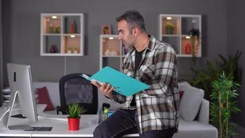 employé riant à la caméra. employé de bureau à domicile regardant la caméra tout en travaillant à l'ordinateur. regardant la caméra et riant avec de la paperasse à la main. video