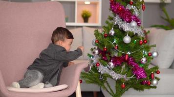 nieuwjaar, baby en grenen. de baby probeert ornamenten op de pijnboom te zetten. het nieuwe jaar vieren. vrolijk en grappig. video