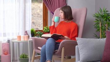 descanso. mujer tomando café mientras lee un libro. mirando por la ventana. video