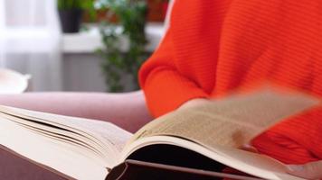 cambiando las páginas del libro, primer plano. la mujer del vestido naranja está cambiando las páginas del libro que está leyendo. video