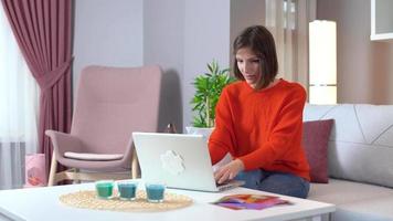 mujer que trabaja en la computadora tomando café. mujer joven relajada usando computadora navegando en las redes sociales, revisando noticias, jugando juegos móviles o enviando mensajes de texto sentados en el sofá. video