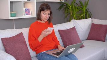 Working by talking on the phone. Woman looking at something on her laptop at home is also talking to someone on the phone. video