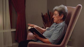 mulher idosa lendo um livro em casa. ele vira as páginas do livro.