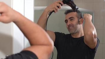 Hair styling with a blow dryer. The man looking at himself in the mirror is styling his hair with a blow dryer. The happy face is striking. video