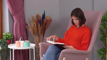 kvinna som läser en bok. kvinna hemma i en orange klänning läser en bok i en rosa fåtölj video