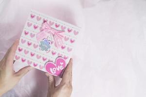 High angle view of two hands holding a gift box with a heart pattern photo